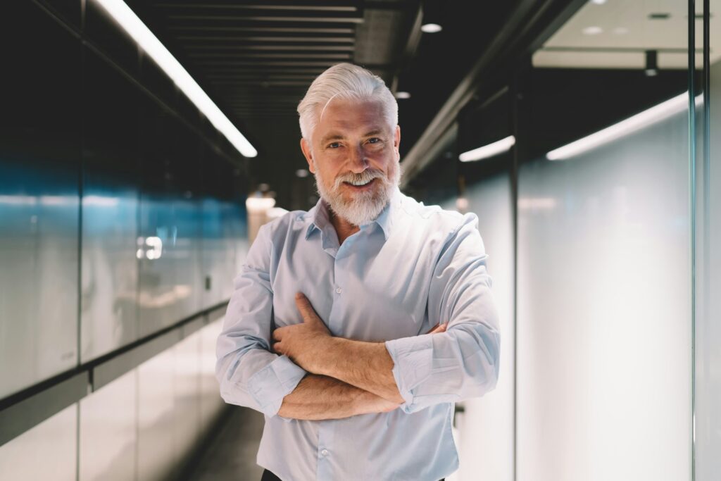 Positive aged businessman smiling and looking at camera in office